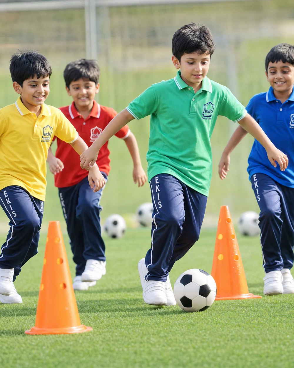 Students in EKIS sports kit dribbling footballs between training cones