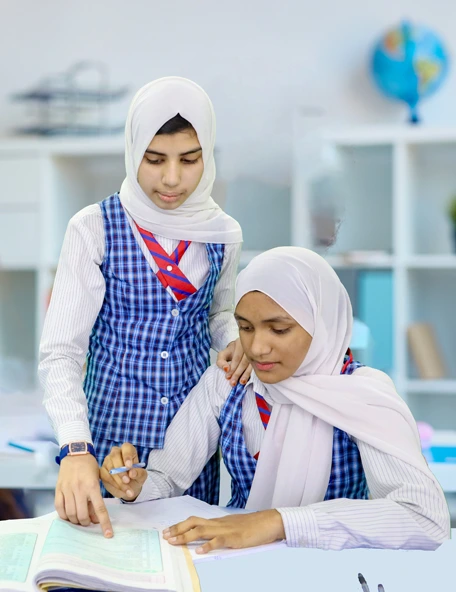 Two senior students in EKIS uniform working through a workbook together at a classroom desk